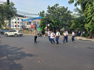 Kapolsubsektor Kayu Awet Membantu Menyeberangkan Anak Sekolah di Jalanan.